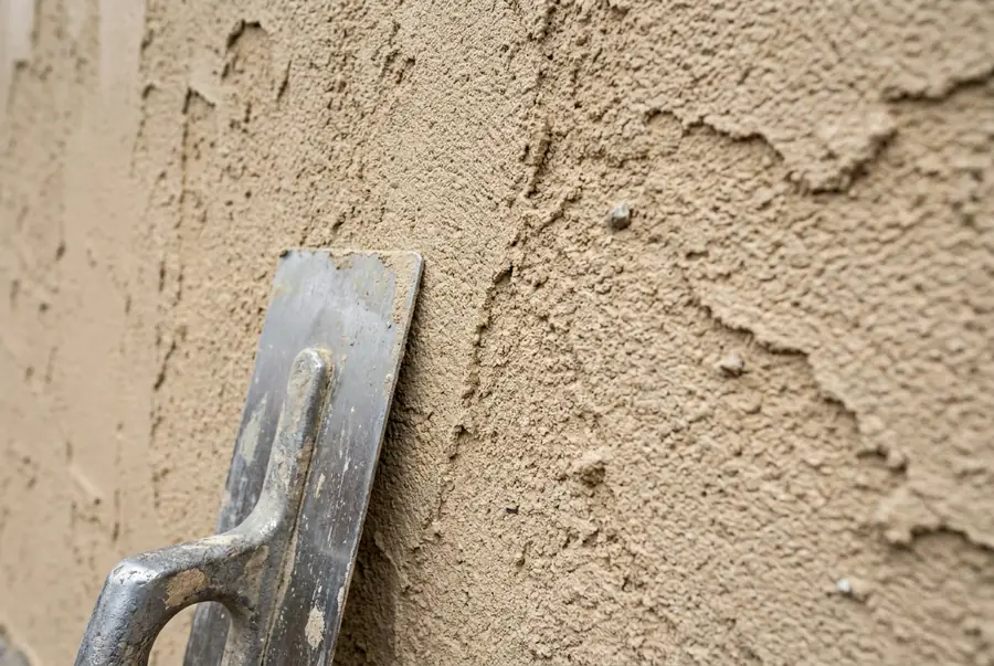 Gros plan sur un enduit écrasé frais, la truelle posée contre le mur
